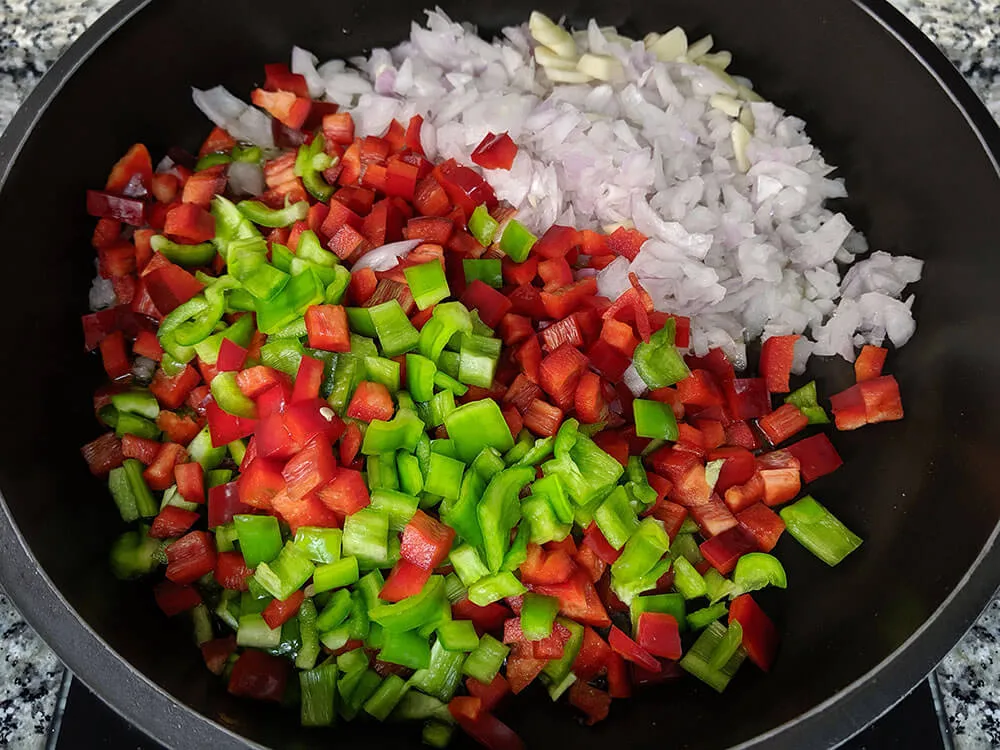 Pimientos, cebolla y dientes de ajo rehogando en sartén.