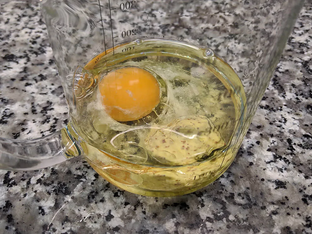 Vaso de batidora con huevo, aceite y mostaza de Dijon.