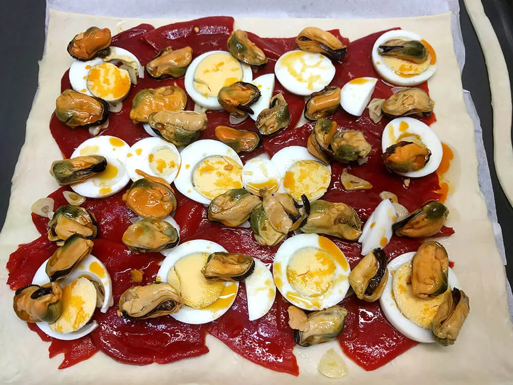 Masa cruda de empanada con pimientos del piquillo, huevo duro y mejillones en escabeche