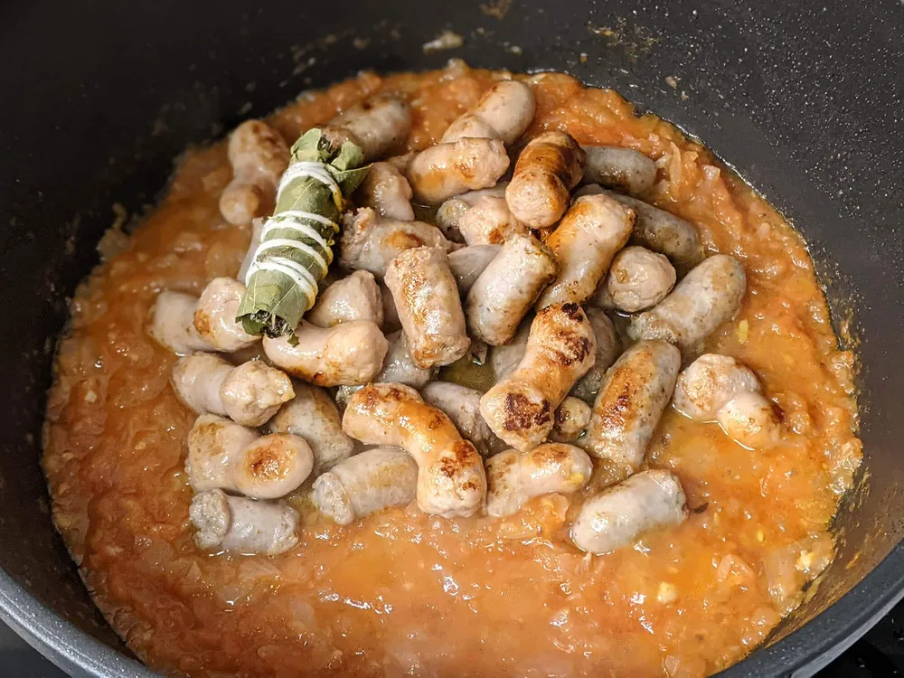 Sofrito de cebolla y tomate con salchichas y atillo de hierbas.