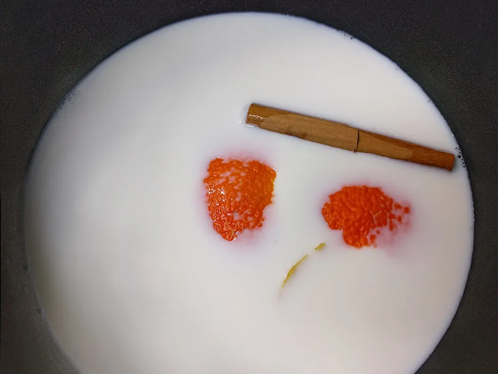 Leche con una rama de canela y cortezas de naranja y limón