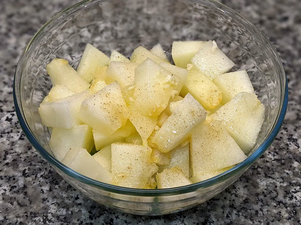 Cuenco con dados de melón, pepino, pimiento verde, cebolla tierna, diente de ajo, dados miga de pan, sal, pimienta blanca y aceite de oliva.