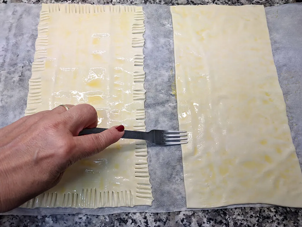 Masa de hojaldre fresca, cortada por la mitad, untada con huevo batido y bordes realizados.