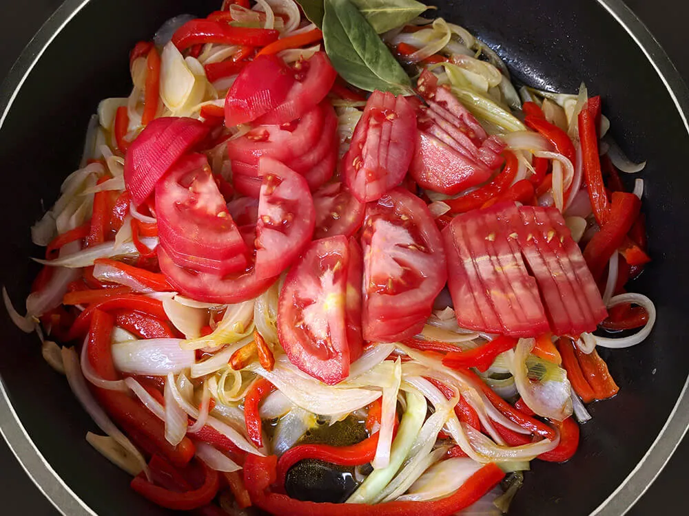 Cazuela con pimiento, cebolla, dientes de ajo y tomate cortados.