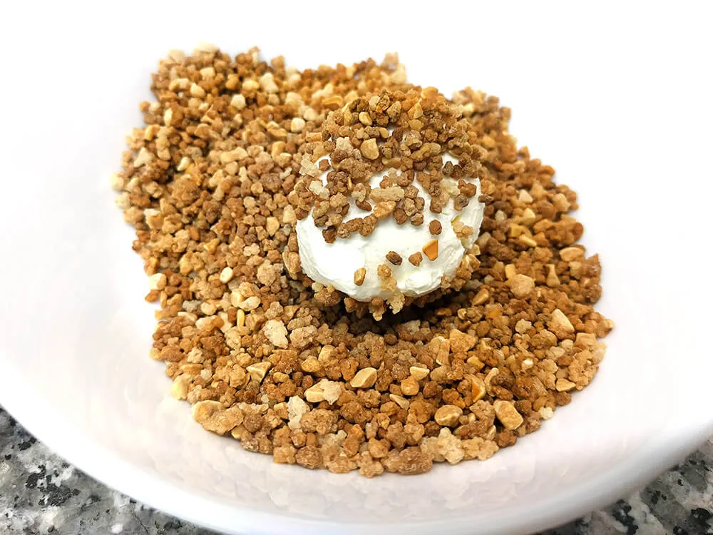 Bola de queso cremoso, rellena de mermelada de tomate y rebozada en crocanti de almendras.