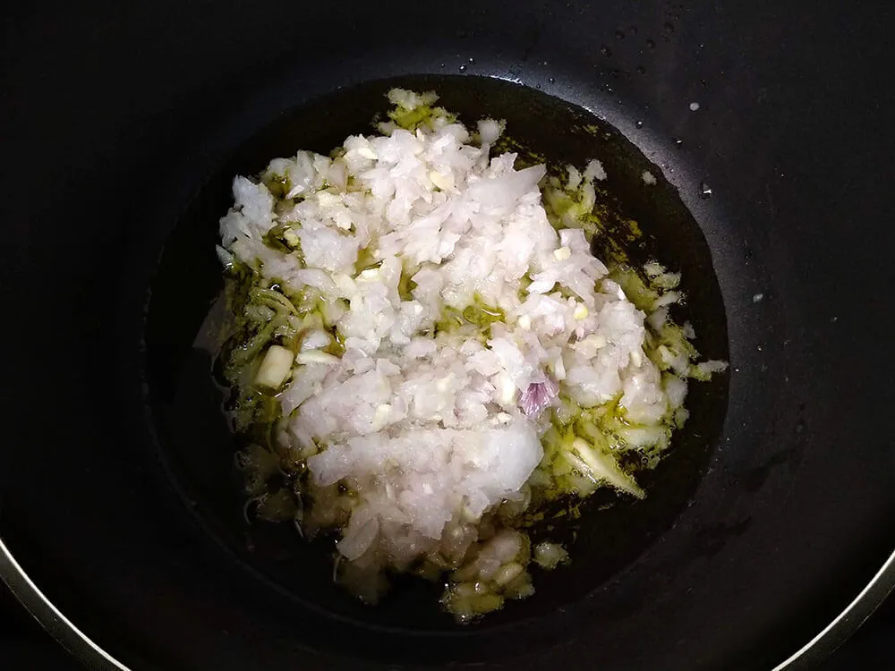 Cebolla y diente de ajo picados en sartén con aceite de oliva.