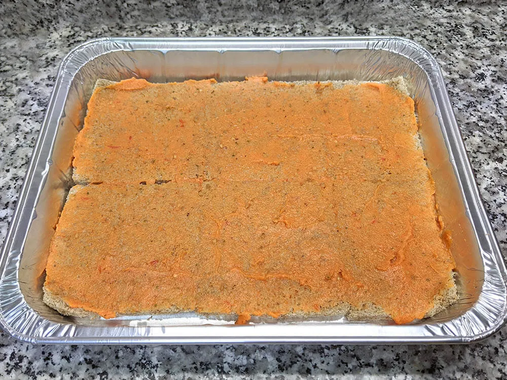 Capa de pan de molde untado con tomate triturado.