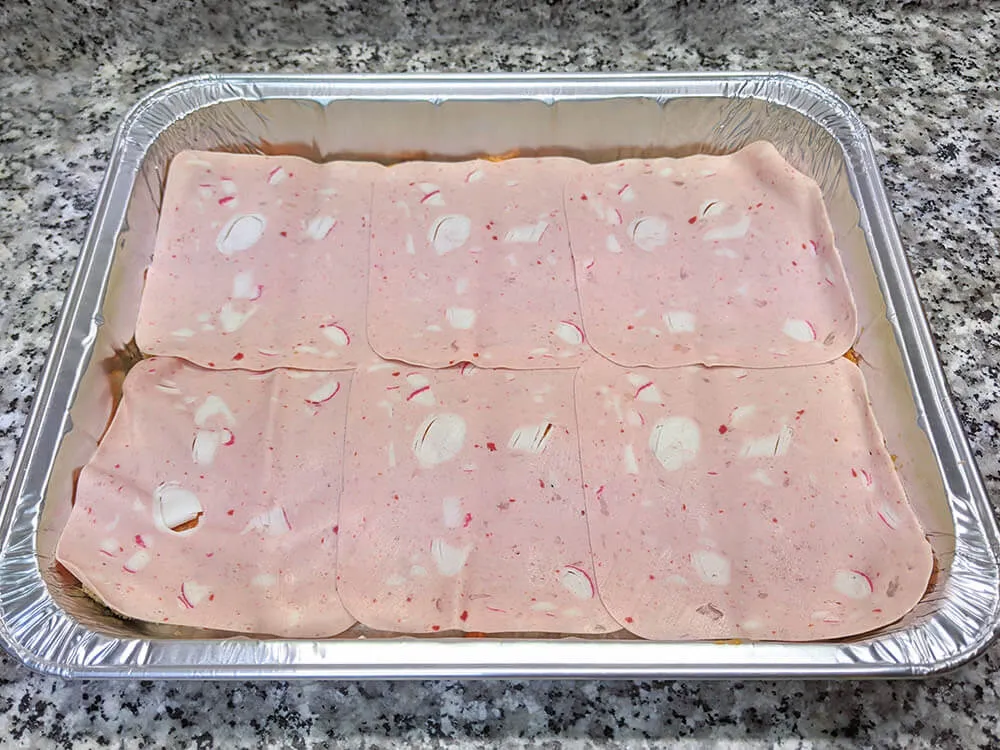 Capa de pan de molde untado con tomate triturado y Delisandwich de cangrejo.