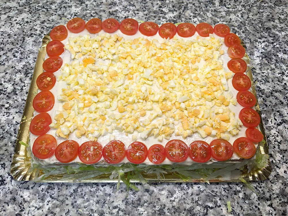 Pastel de pan de molde untado con mayonesa, lechuga, cherrys y huevo duro picado.
