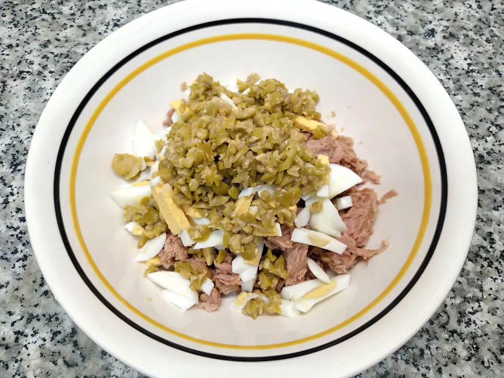 Cuenco con atún, huevos cocidos picados y olivas picadas.
