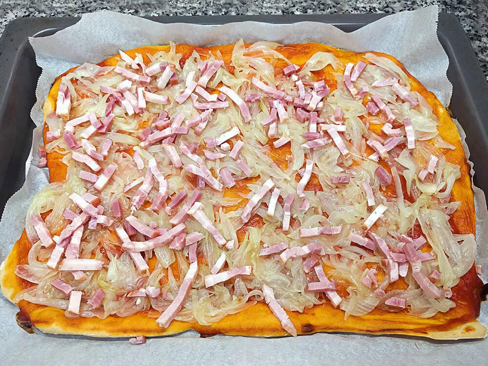 Base de pizza con cebolla frita y bacon.